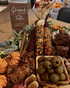 Thanksgiving table with corn, olives, bread, and decorative foliage for festive gathering.