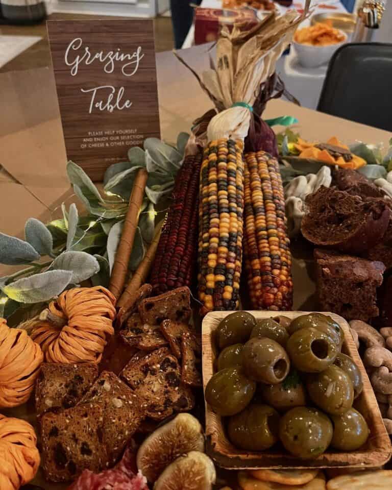 Thanksgiving table with corn, olives, bread, and decorative foliage for festive gathering.