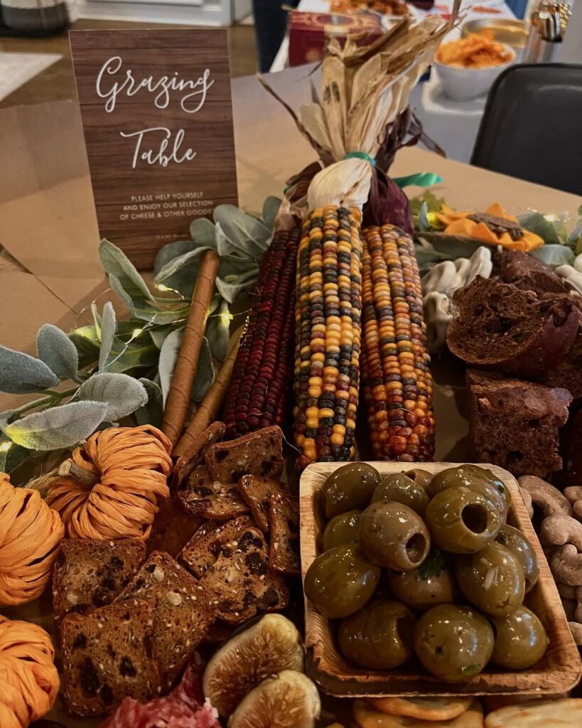 Thanksgiving table with corn, olives, bread, and decorative foliage for festive gathering.