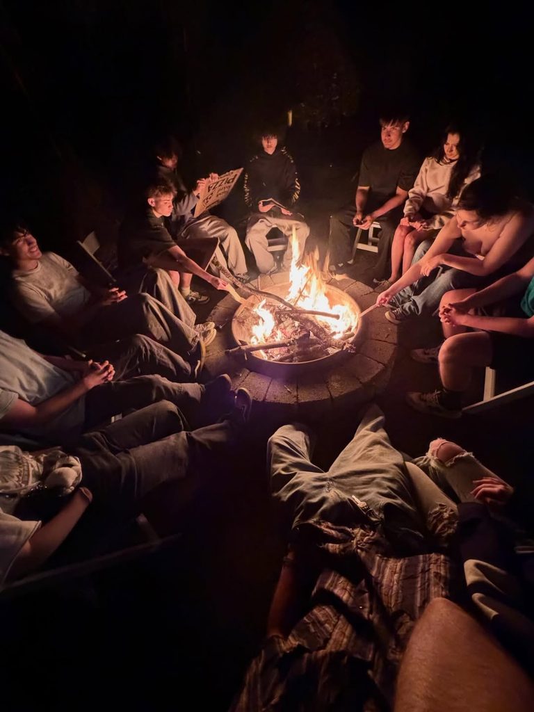 Group of friends sitting around a bonfire at night, enjoying a cozy outdoor gathering.