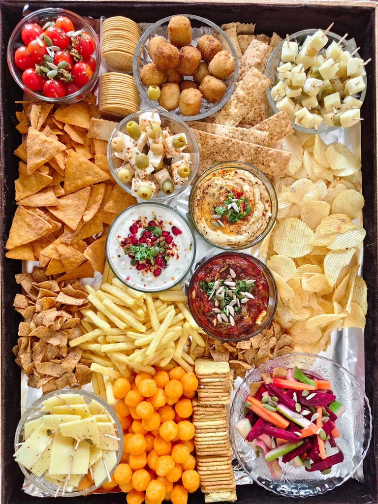 Colorful Friendsgiving cheese and snack platter with dips, fruits, and crackers.