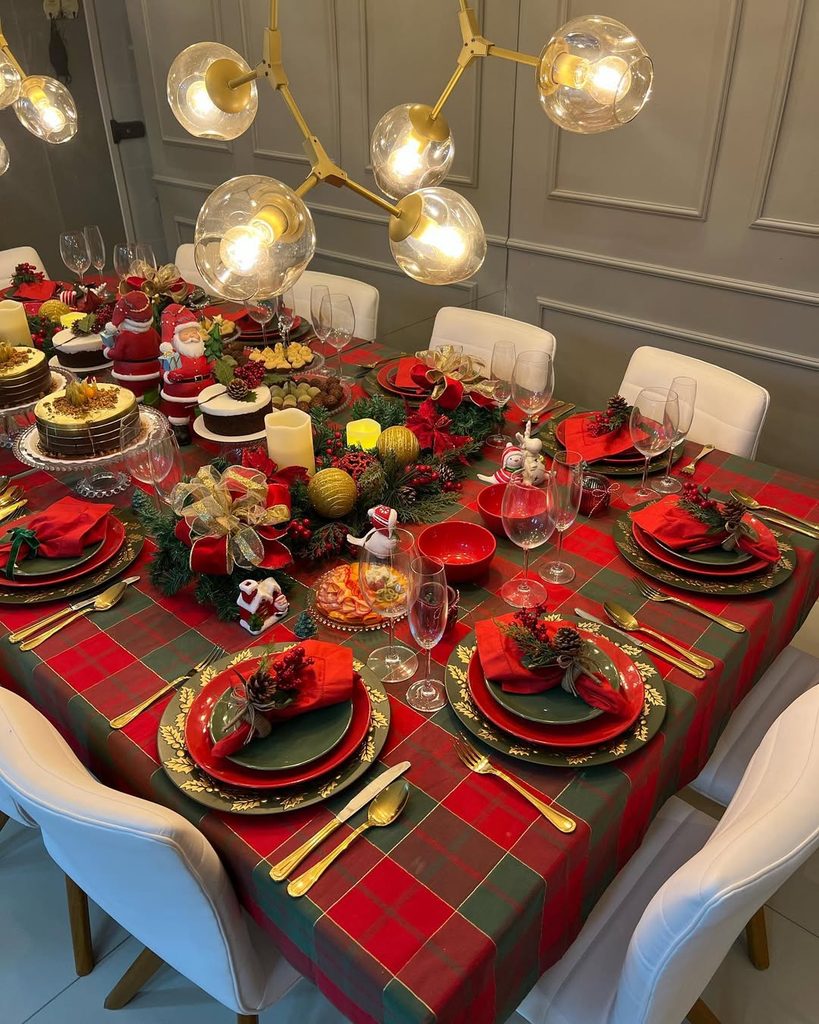 Festive Christmas dinner table with red and green decor, candles, and holiday ornaments.