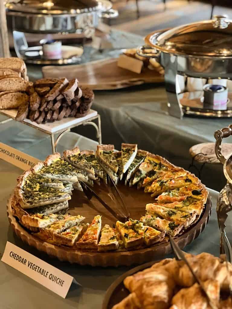 Cheddar vegetable quiche slices on a round wooden platter at a fall luncheon buffet.