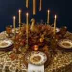 Elegant Thanksgiving table setting with gold accents, candles, and autumn foliage.