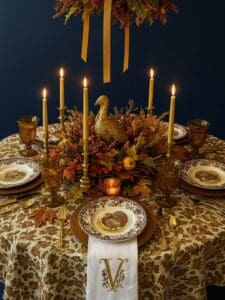 Elegant Thanksgiving table setting with gold accents, candles, and autumn foliage.