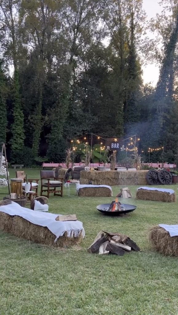 Cozy outdoor bonfire party setup with string lights, hay bales, and seating area.