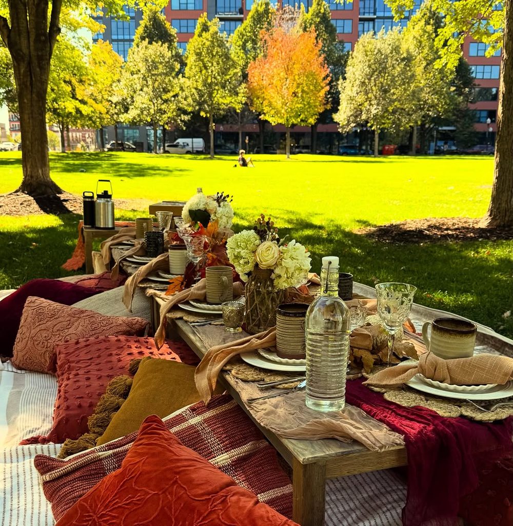 Friendsgiving outdoor picnic with autumn decor, flowers, and cozy table setting in park.