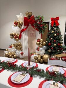 Festive Christmas baby shower table with gold, white, and red decorations and a decorated Christmas树.