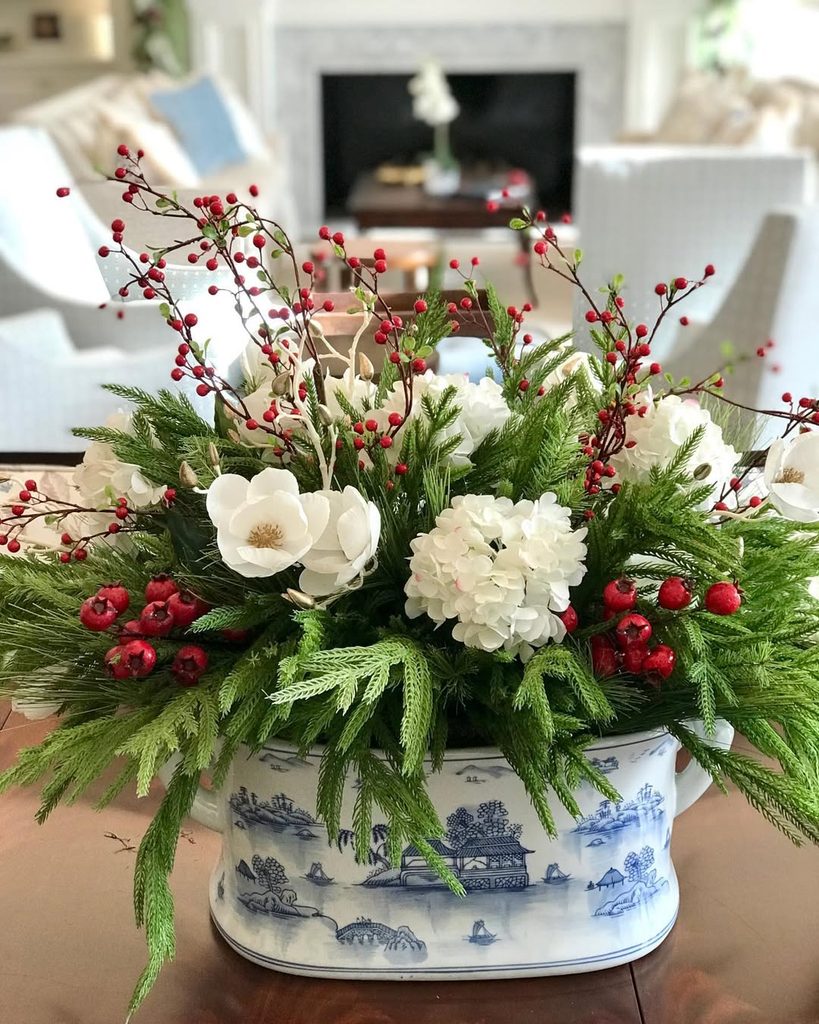 Festive Christmas floral arrangement with white flowers and red berries in a blue and white ceramic.