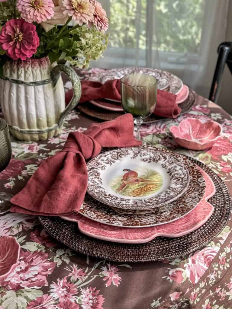 Vintage Thanksgiving tablescape with floral tablecloth, layered plates, and pink napkins.