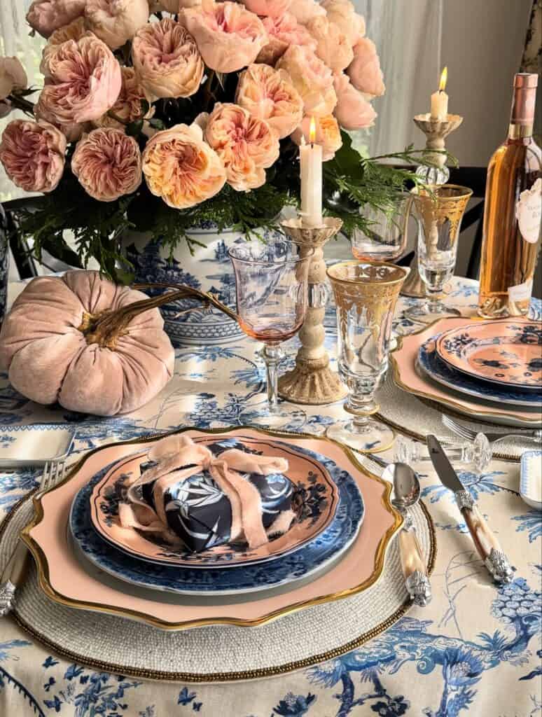 Elegant Thanksgiving table setting with pink roses, candles, and blue and pink dinnerware.