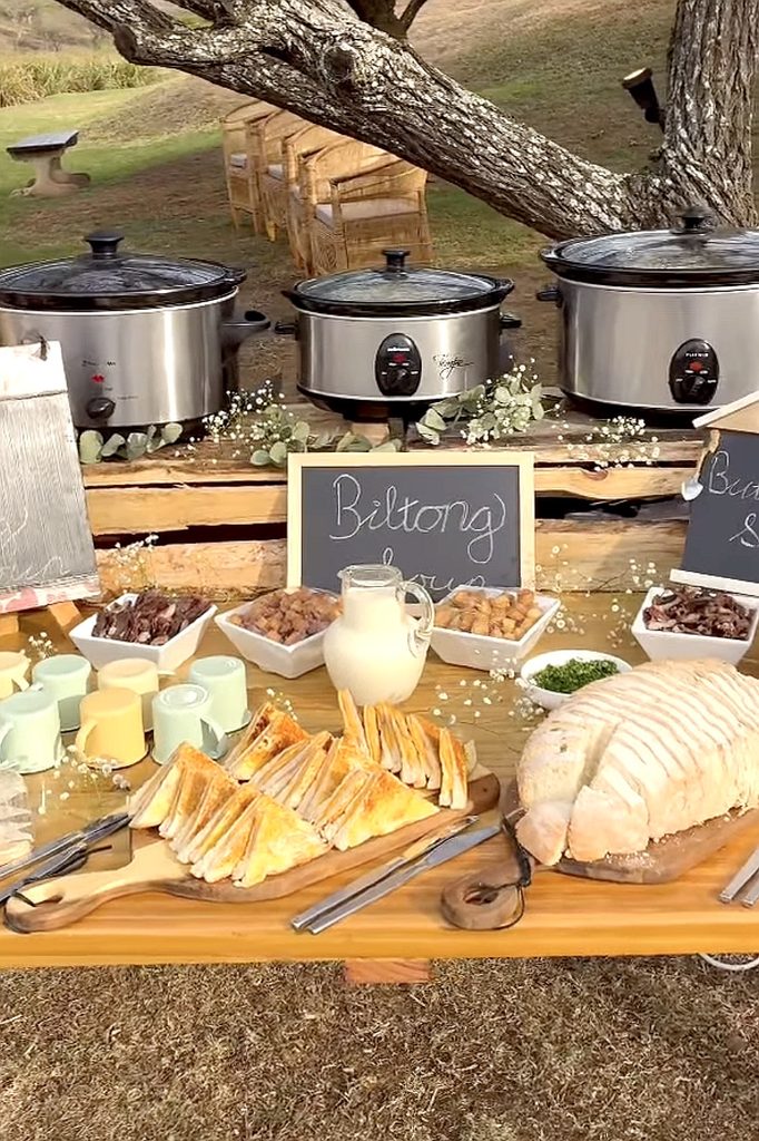 Cozy outdoor soup bar with bread, cheese, and toppings under a tree for a party.