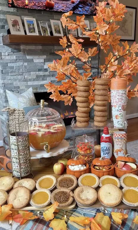 Autumn-themed table with apple cider, cookies, and fall decorations for a cozy gathering.