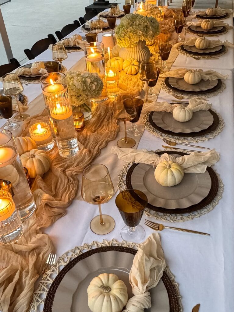 Elegant Thanksgiving table setting with white pumpkins, candles, and floral centerpieces.