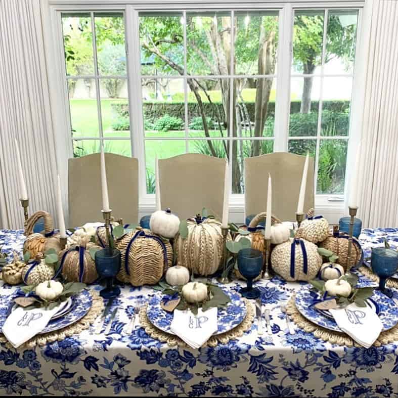 Elegant Thanksgiving table with white pumpkins, blue accents, and candles in front of a large window.