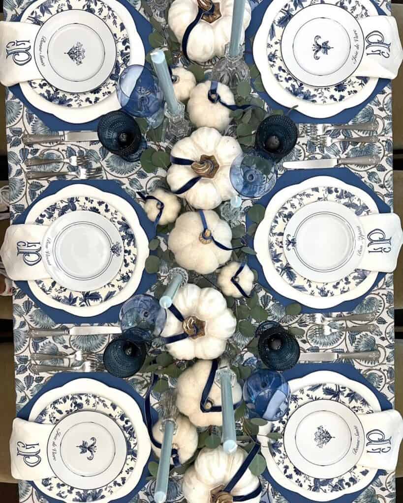 Elegant blue and white Thanksgiving table setting with pumpkins and candles.