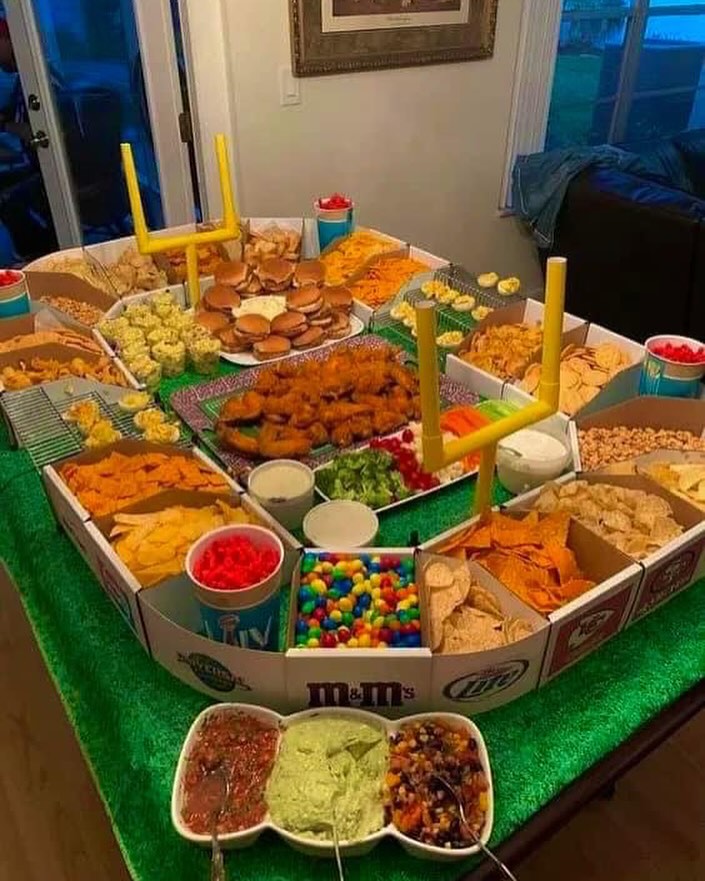 Friendsgiving party table with snacks, dips, and colorful candies on a green tablecloth.