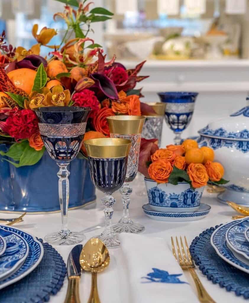 Elegant Thanksgiving table setting with blue and gold dishware and vibrant floral centerpiece.