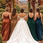 Elegant bridesmaids in fall-colored dresses with a bride in a white gown outdoors.