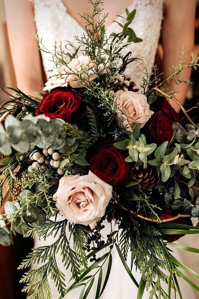 Elegant winter wedding bouquet with red and blush roses, greenery, and pinecones.
