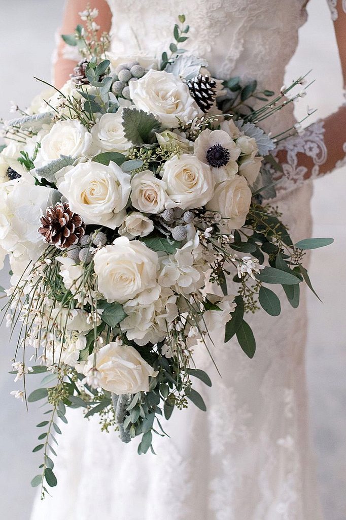 Elegant winter wedding bouquet with white roses, pinecones, and greenery.