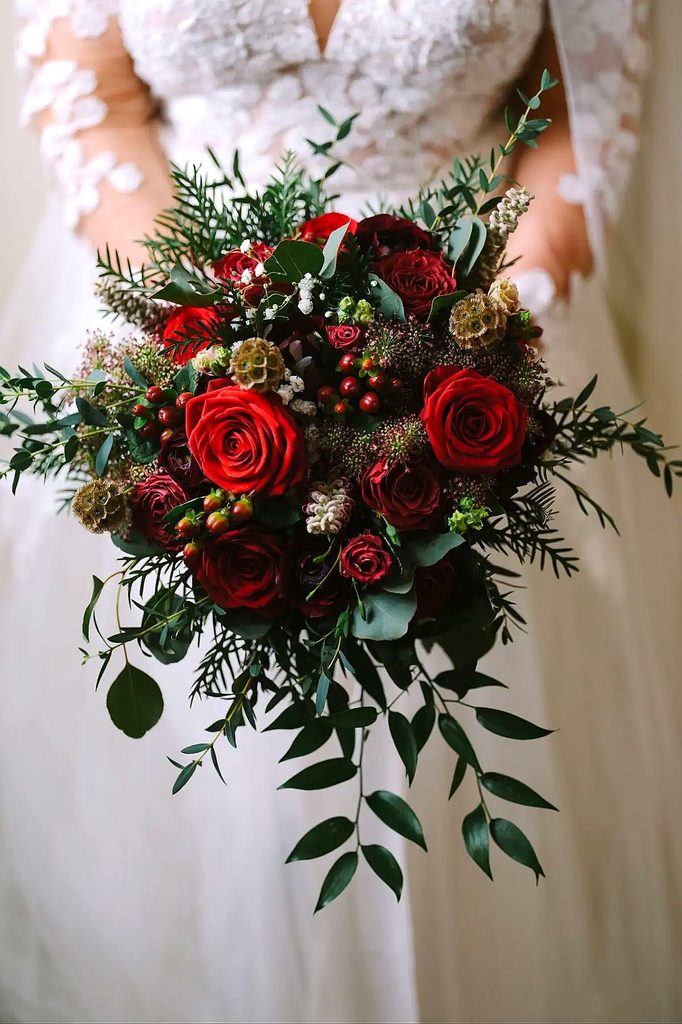 Elegant winter wedding bouquet with red roses, greenery, and berries.