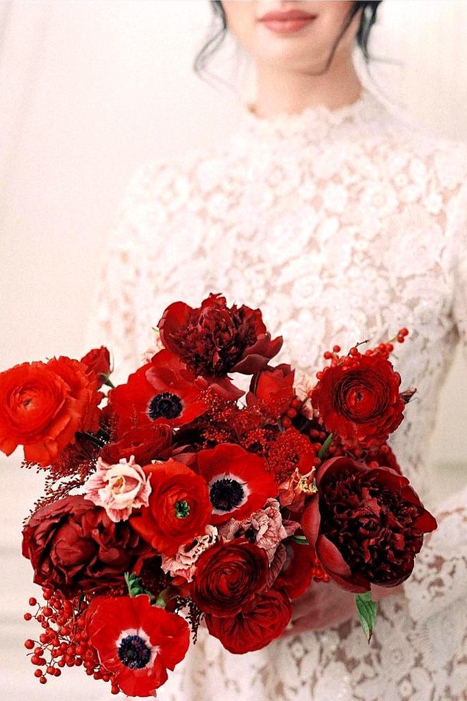 Elegant bride holding a lush red wedding bouquet with roses and anemones.