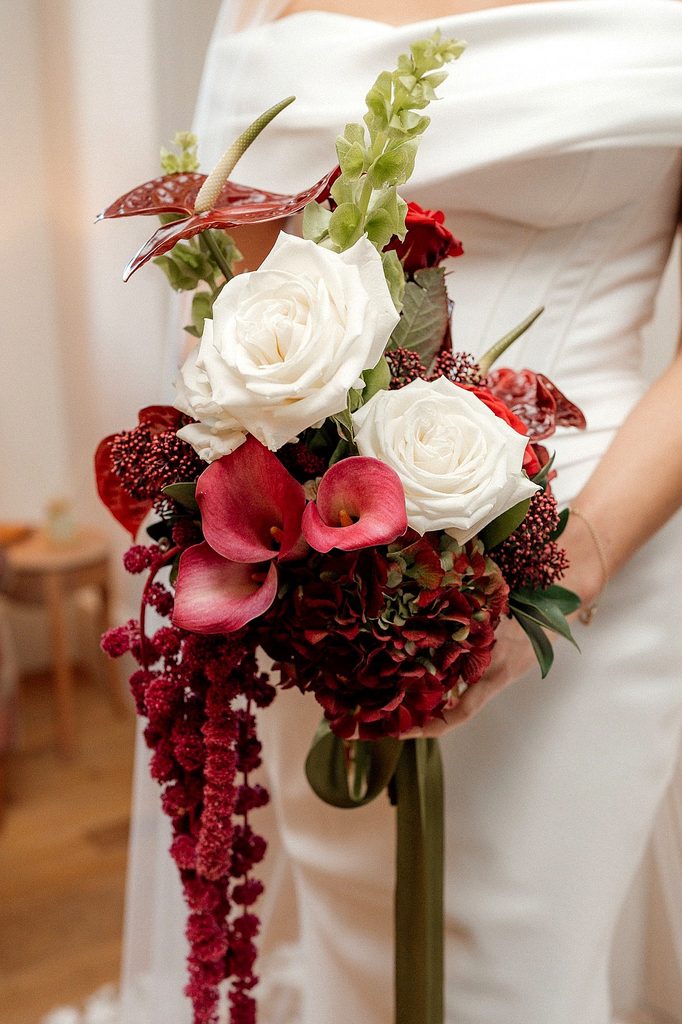 Elegant winter wedding bouquet with white roses, red calla lilies, and greenery.