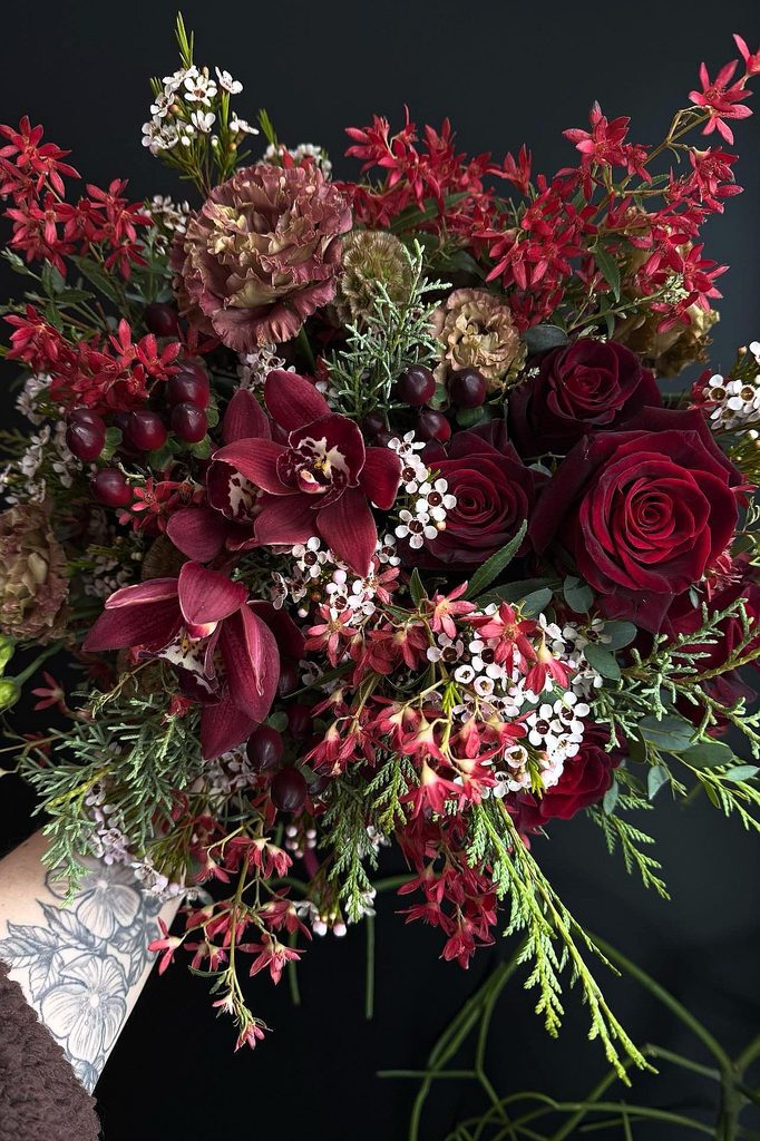 Elegant winter wedding bouquet with deep red roses, orchids, and greenery.