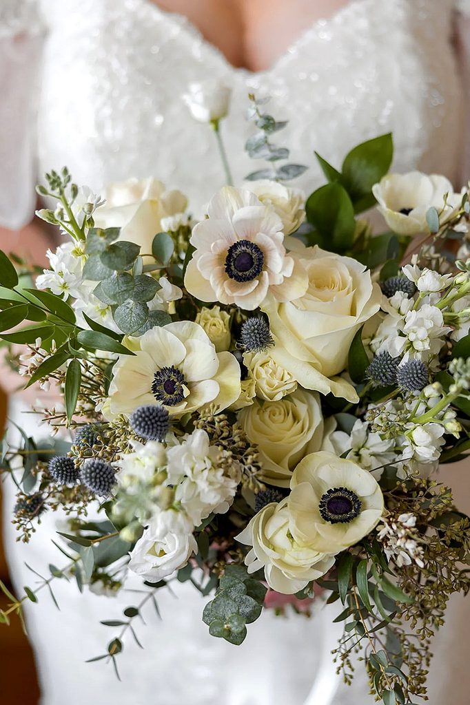 Elegant winter wedding bouquet with white roses, anemones, and greenery.