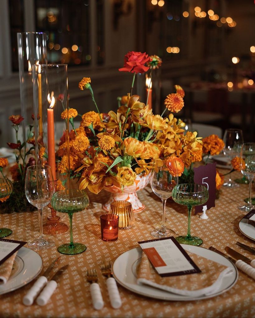 Elegant fall wedding table with orange and yellow floral centerpiece, candles, and glassware.