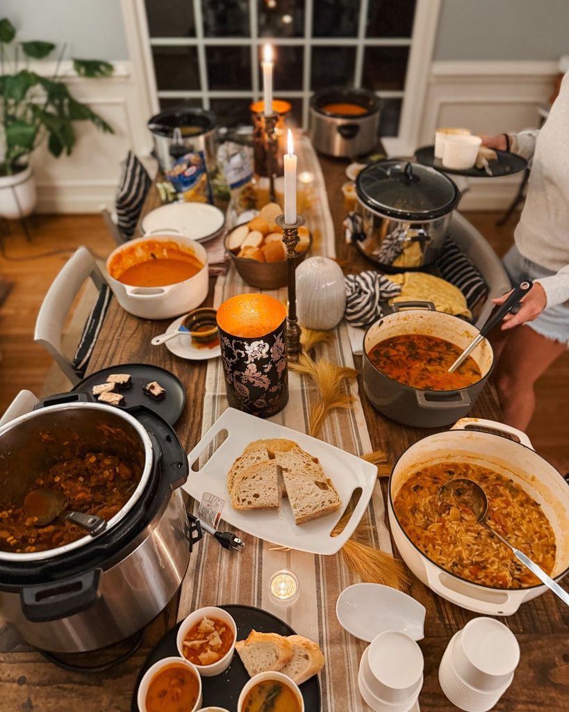 Cozy fall or winter soup luncheon with various bowls of soup, bread, and candles on a wooden table.