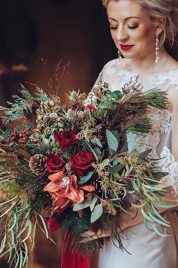 Elegant bride holding a lush winter wedding bouquet with red roses and greenery.