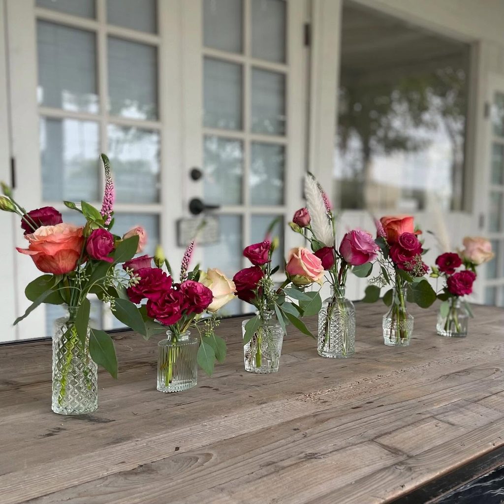Elegant floral arrangement with pink and red roses in vintage glass vases on wooden table.