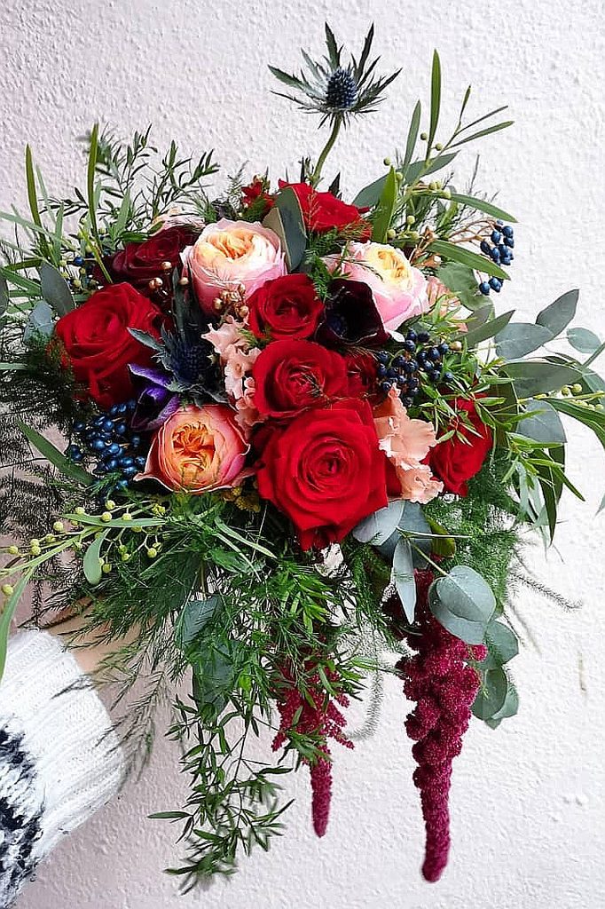 Elegant winter wedding bouquet with red roses, pink peonies, and greenery.