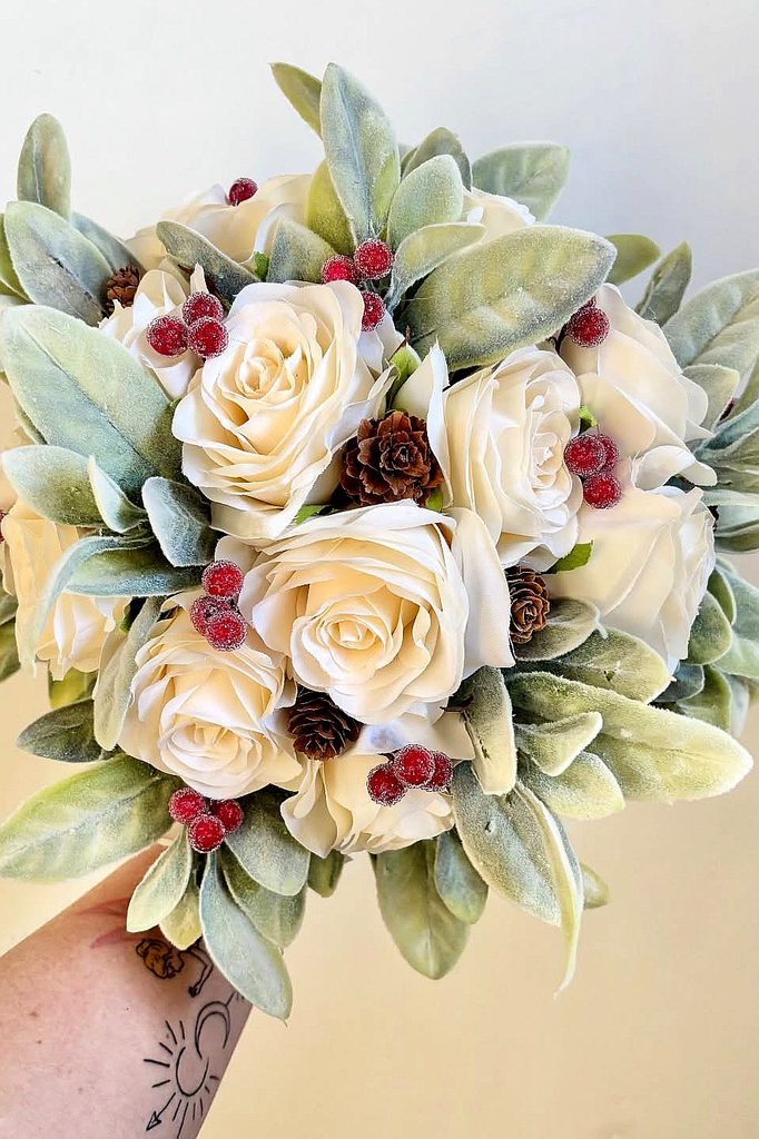 Elegant winter wedding bouquet with white roses, pinecones, and frosted greenery.