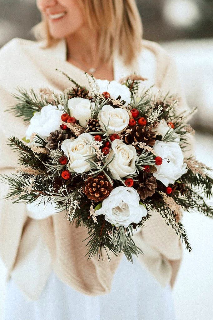 Elegant winter wedding bouquet with white roses, pinecones, and red berries.